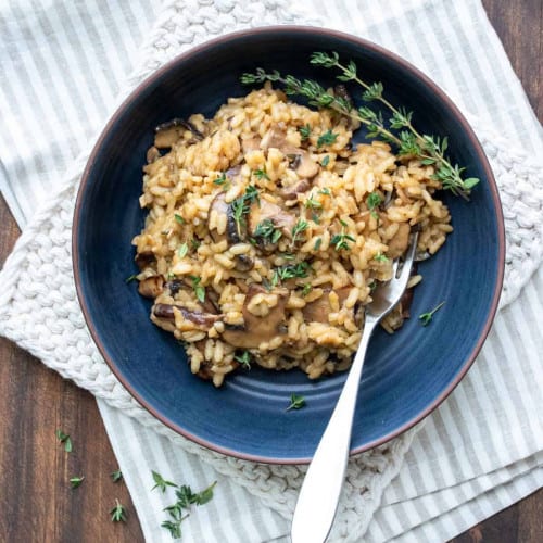 overhead of vegan mushroom risotto in a blue dish with a fork in it.