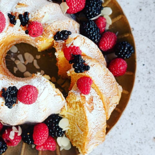 A slice of pound cut and halfway out from the whole cake topped with berries.