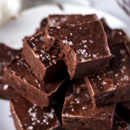 Stack of fudge cut into cubes on a white plate for a potluck.