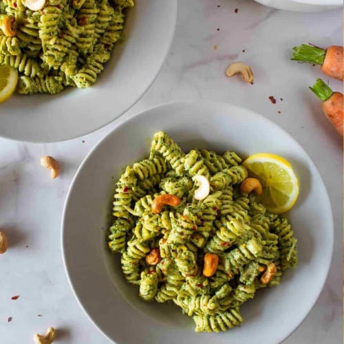 Bowl of pesto pasta with cashews and a lemon slice.