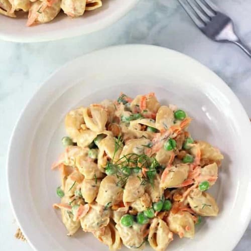 Bowl of creamy pasta with peas and carrots on a white and gray countertop.