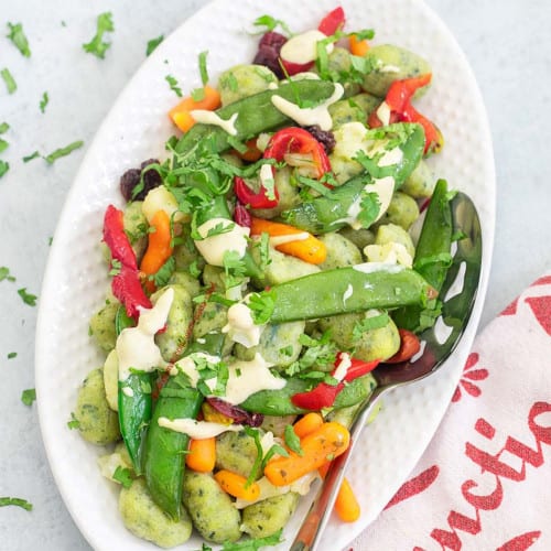 Pasta salad with snap peas, peppers and carrots on an oval platter.