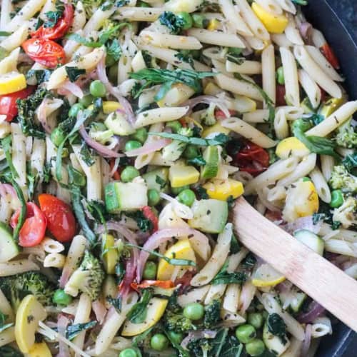 Pot of pasta primavera with yellow squash and veggies on the table.