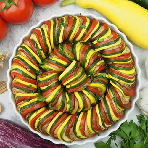 Round casserole dish with alternating yellow squash, green zucchini and red tomatoes.