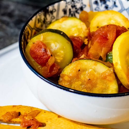 Bowl of squash and tomatoes on the table with a slotted spoon.