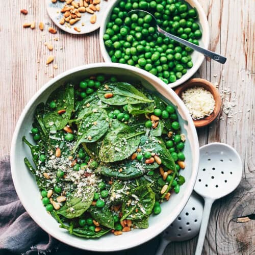 Pea and Pesto Spinach Salad in a bowl on a table with spoons.