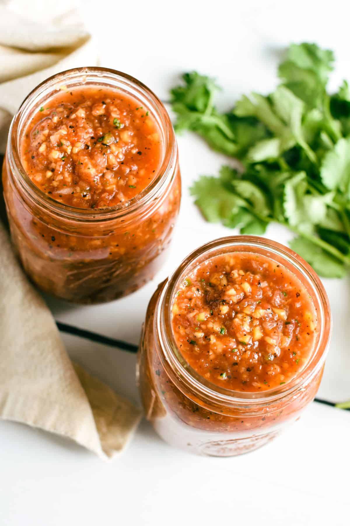 overhead of salsa in two mason jars and some cilantro on the table.