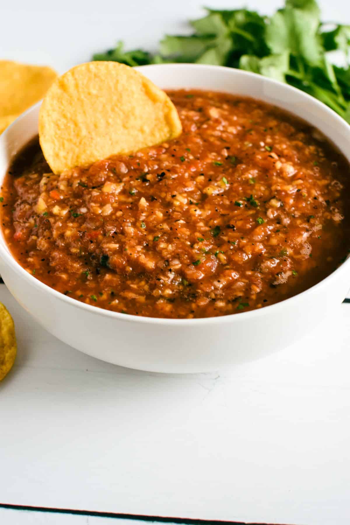 front view of salsa in a white bowl with a chip in it.