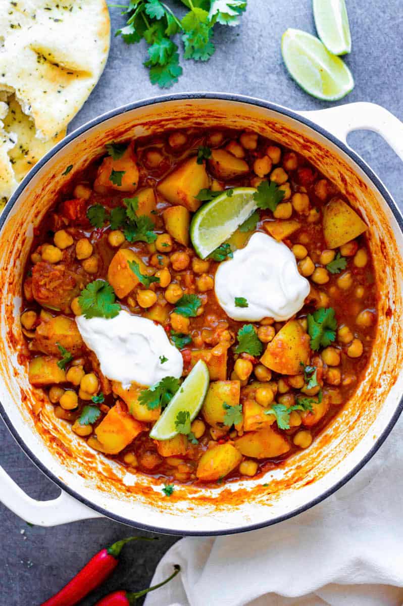 Chickpea and potato curry in a white Dutch oven topped with two dollops of sour cream, and fresh cilantro.