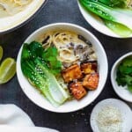 Two white bowls filled with vegan ramen, topped with fried tofu, bok choy, and sesame seeds.