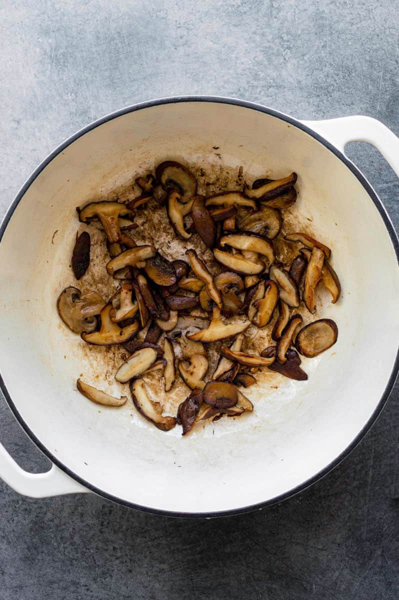 Frying fresh shiitake mushrooms in a white Dutch oven.