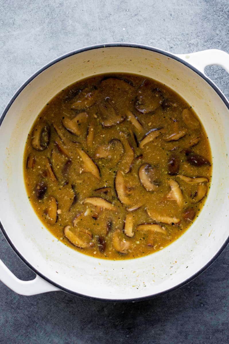 Mushroom broth for the ramen cooking in a white Dutch oven.