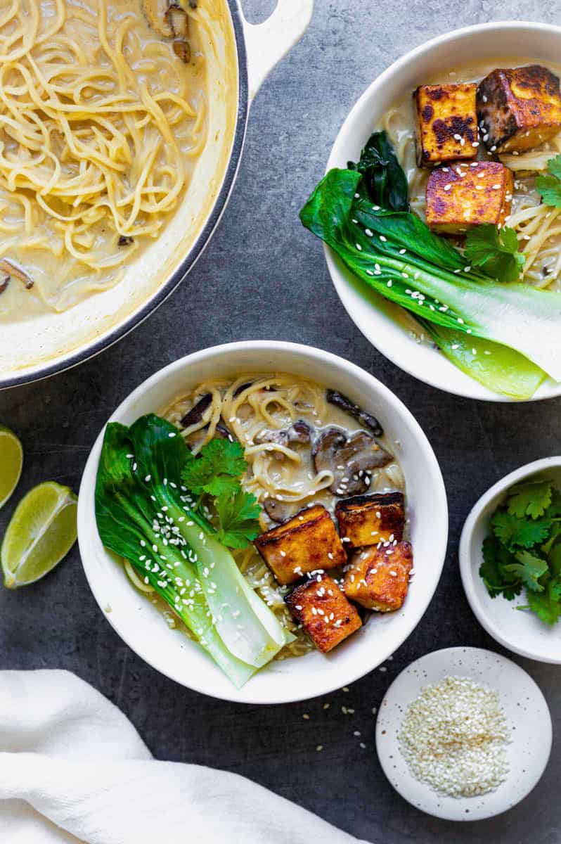 Two white bowls filled with vegan ramen, topped with fried tofu, bok choy, and sesame seeds.