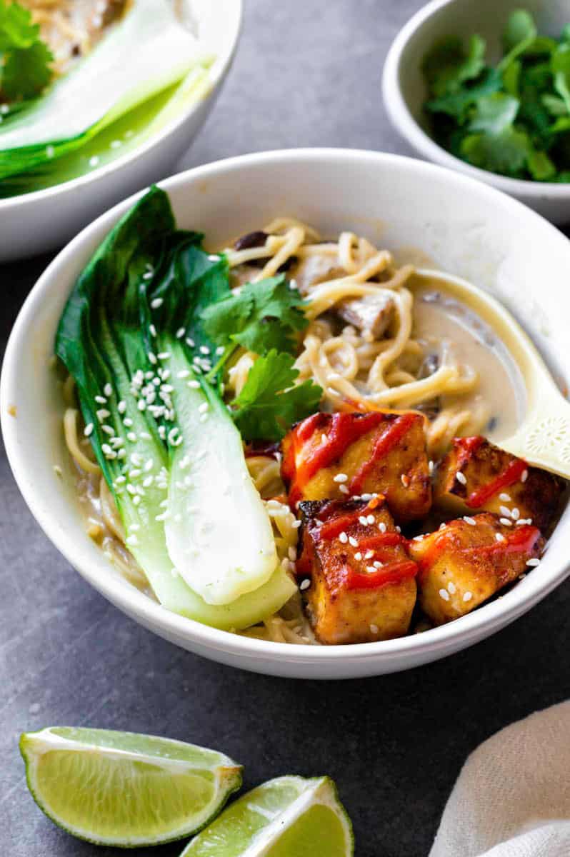 Vegan tofu ramen served in a white bowl, topped with bok choy, fresh cilantro, and sesame seeds.