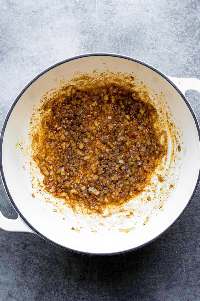 Frying onion and garlic with spices in a white Dutch oven.