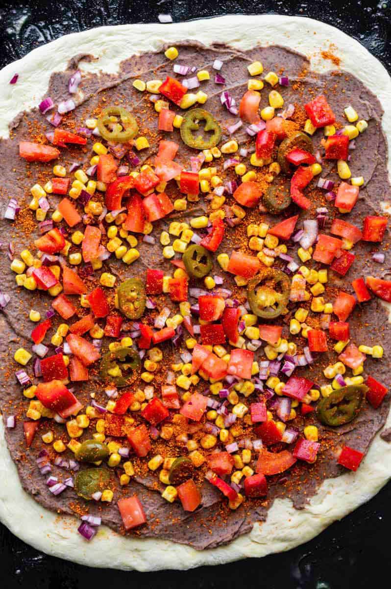 Pizza dough layered with refried beans and chopped vegetables and sprinkled with taco seasoning.