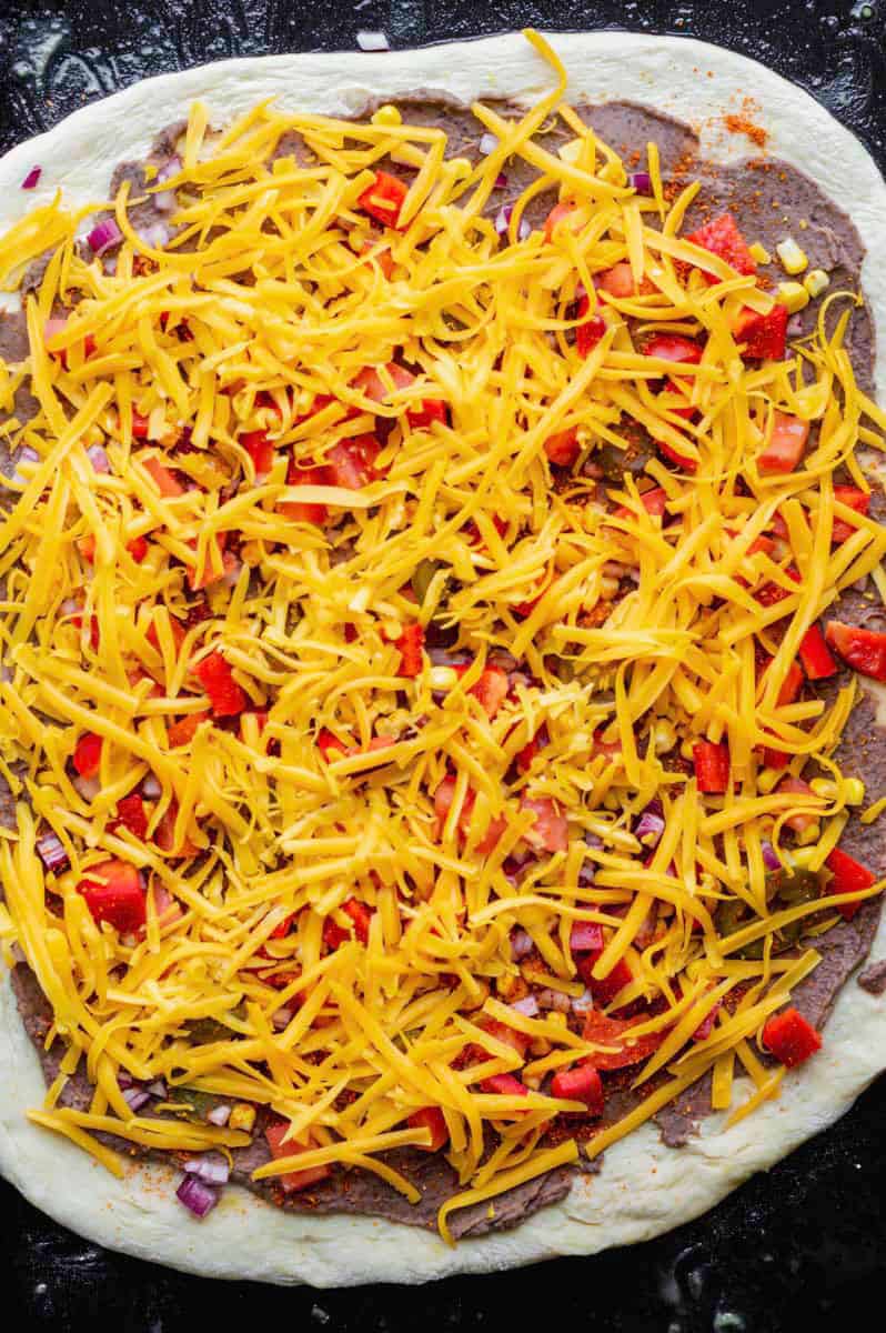 Uncooked vegetarian mexican pizza on a black baking sheet.