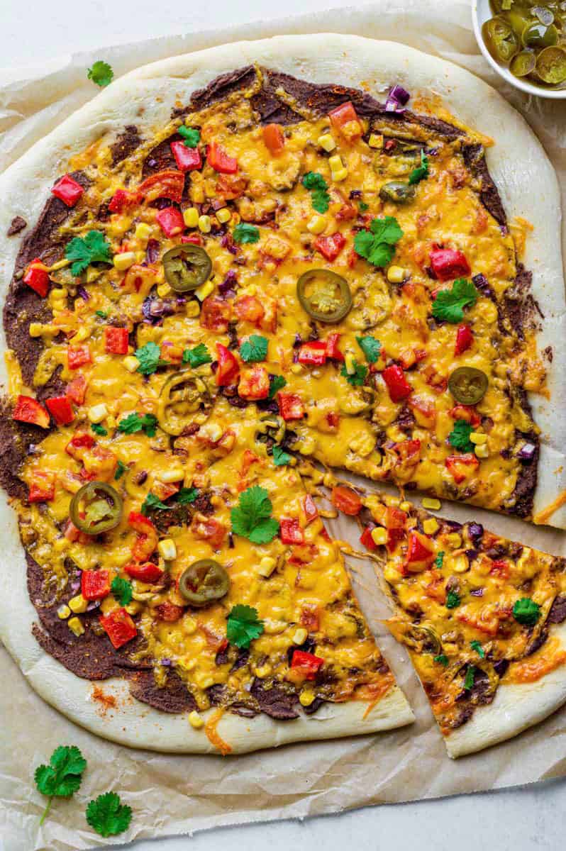 Vegetarian Mexican Pizza on a piece of brown parchment paper. The pizza is topped with fresh cilantro and pickled jalapenos.