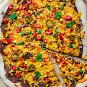 Vegetarian Mexican Pizza on a piece of brown parchment paper. The pizza is topped with fresh cilantro and pickled jalapenos.