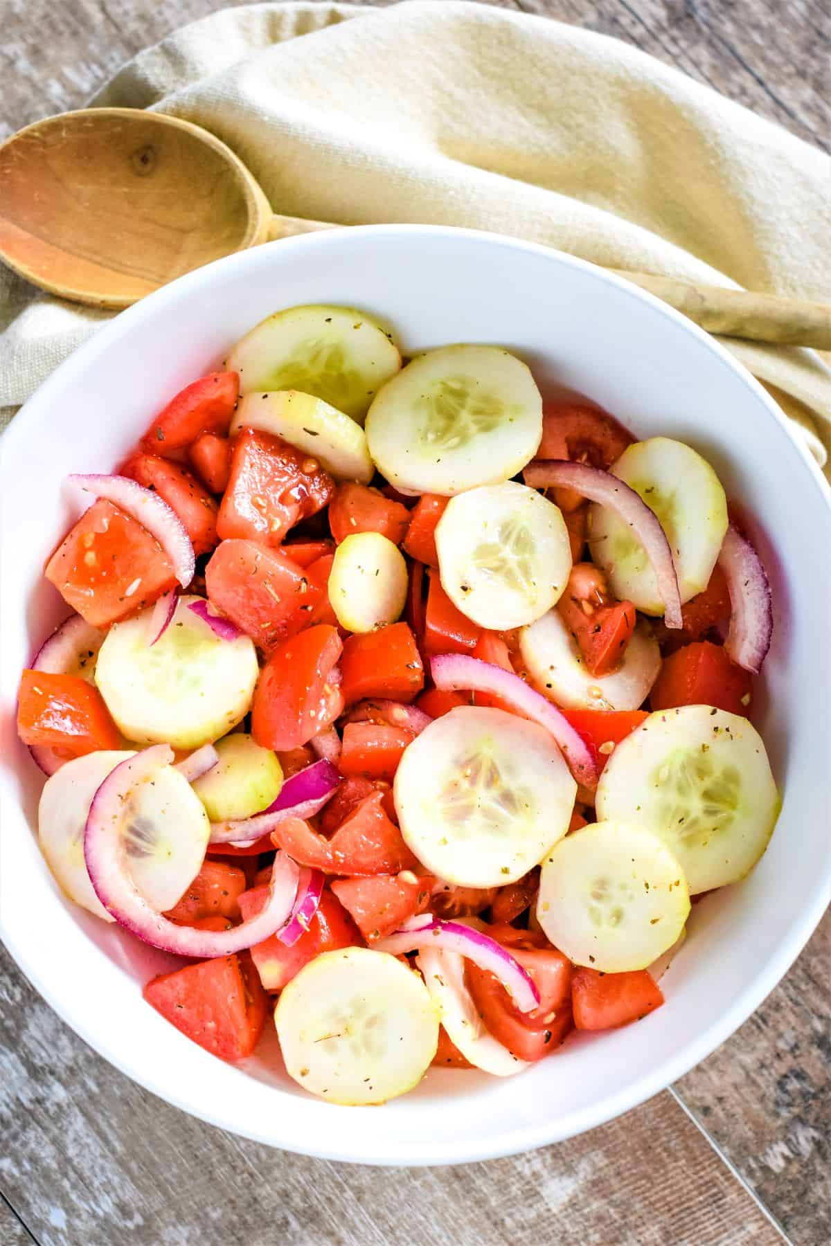 overhead of salad in a large white bowl with a wooden spoon on a kitchen napkin behind it.