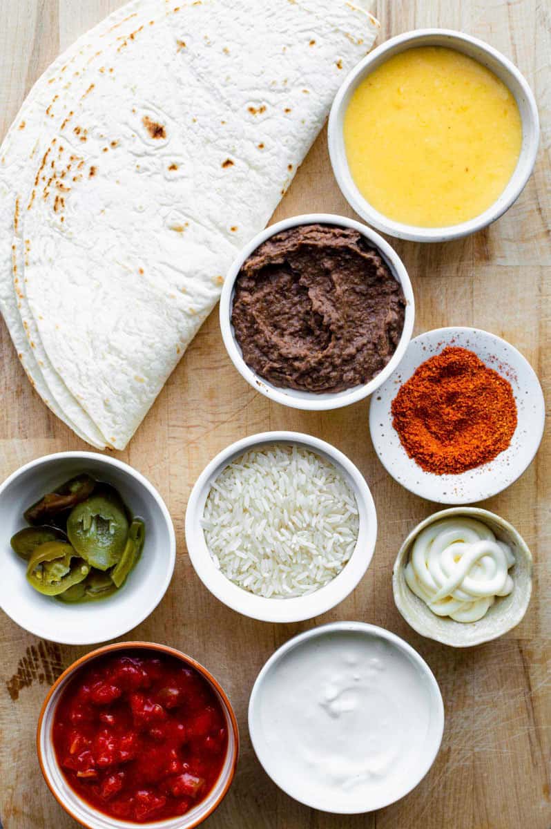 Gathered ingredients placed on a wooden cutting board for making our cheesy bean and rice burrito recipe.