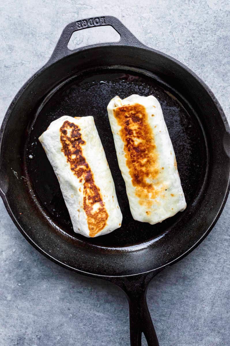 Frying two burritos in a black cast-iron skillet.