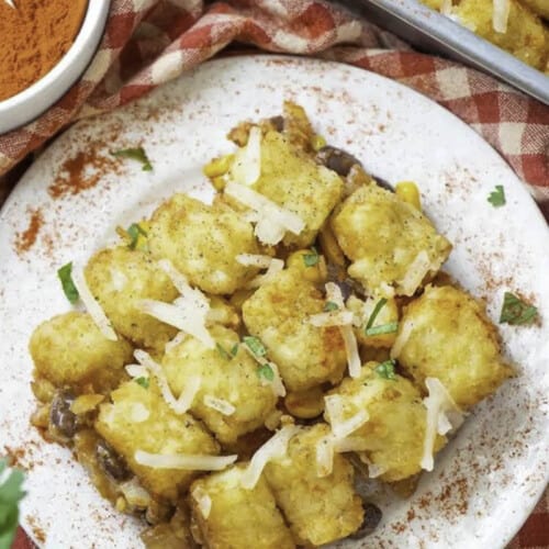 A piece of vegan tater tots casserole served on a white plate and sprinkled with paprika.