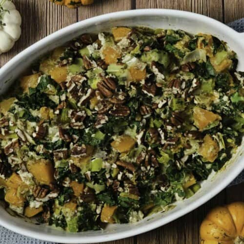 Butternut squash casserole in a casserole dish with small pumpkins nearby.