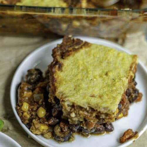 Vegan tamale pie served on a small white plate with a casserole dish in the background.