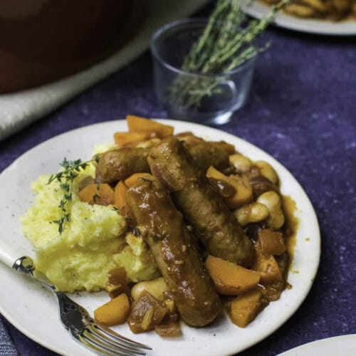 Vegan sausage casserole with polenta served on a white plate with a small jar filled with thyme in the background.