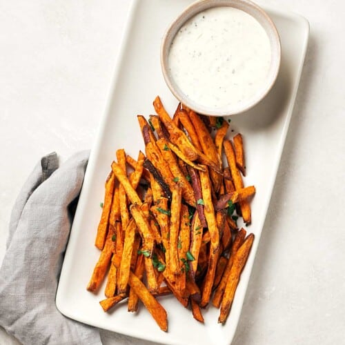 overhead of sweet potato fries on a white serving platter with a side of dipping sauce.