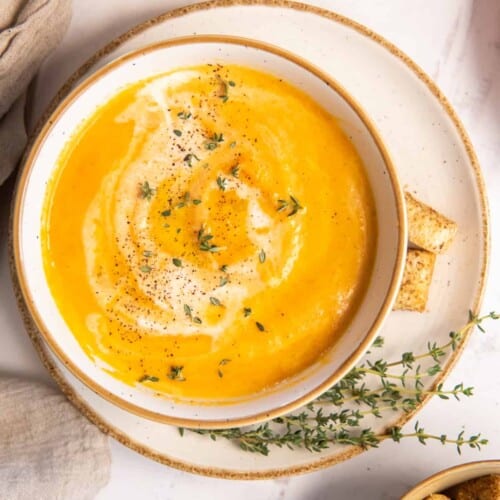 overhead of carrot soup in a bowl on a plate with rosemary garnish on the plate.