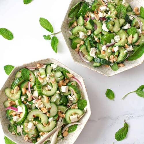 overhead of two bowls of cucumber feta mint salad with mint garnish around.