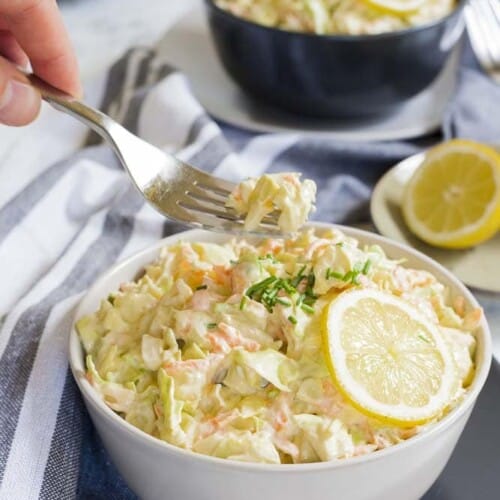 hand scooping up some vegan coleslaw with a fork out of a bowl.