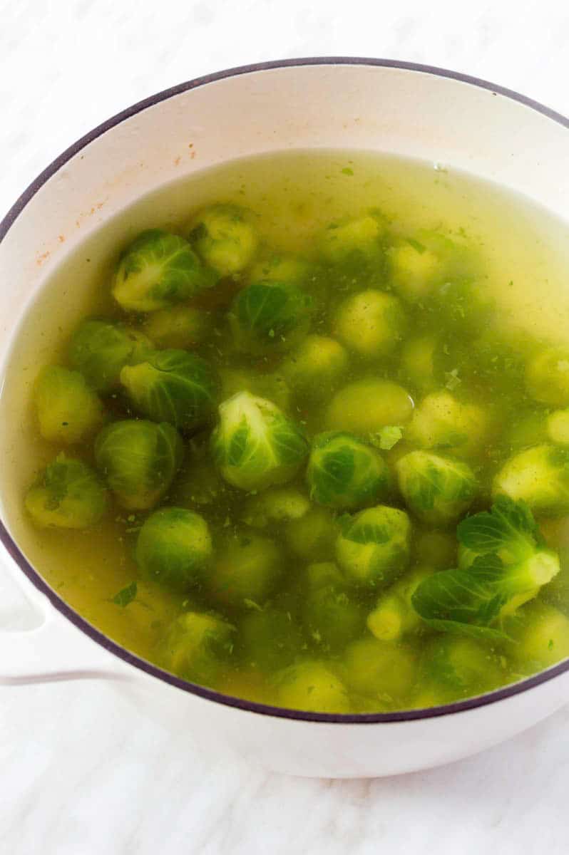 Blanching frozen brussels sprouts in hot water in a white Dutch oven.