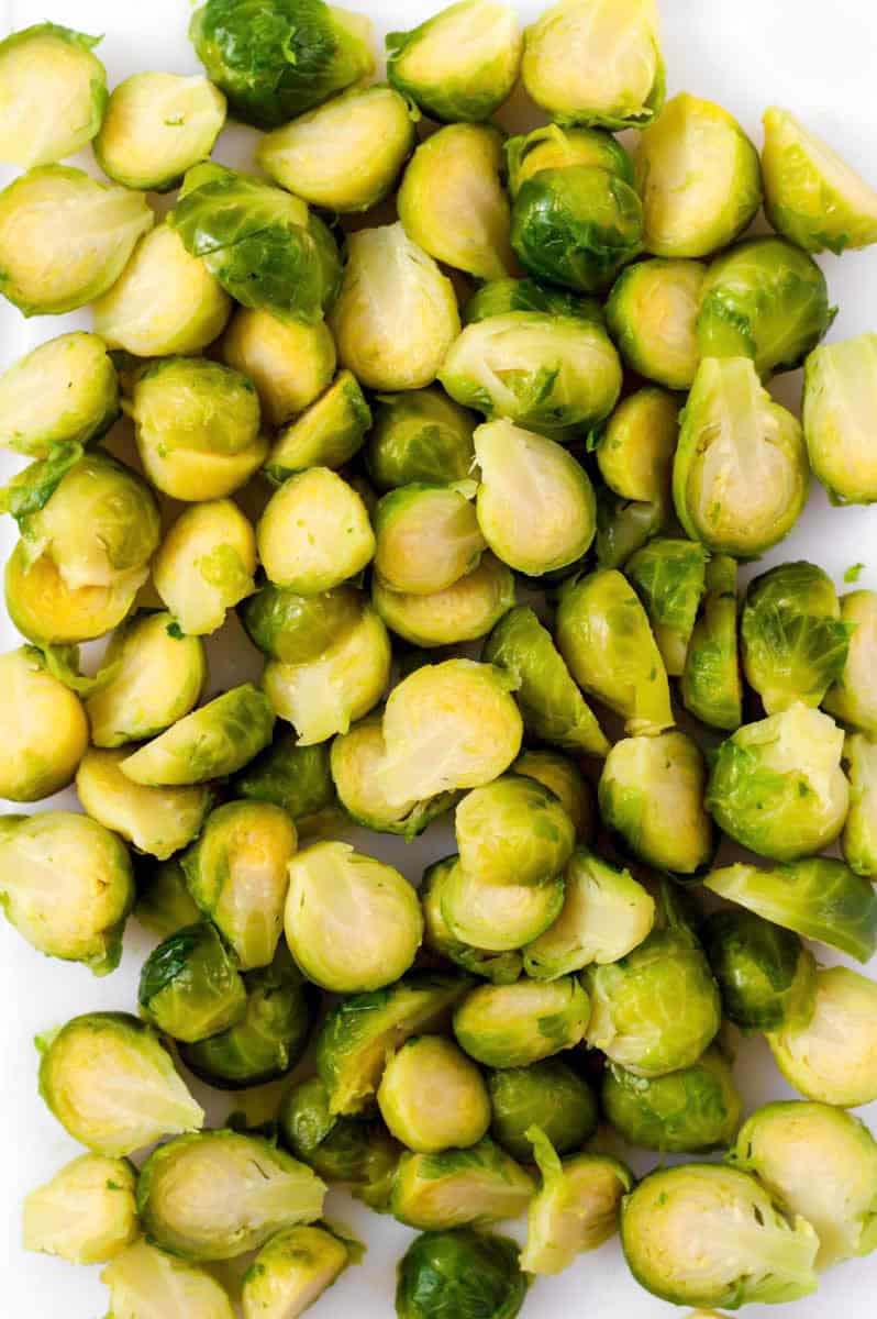 Halved brussels sprouts on a white cutting board.