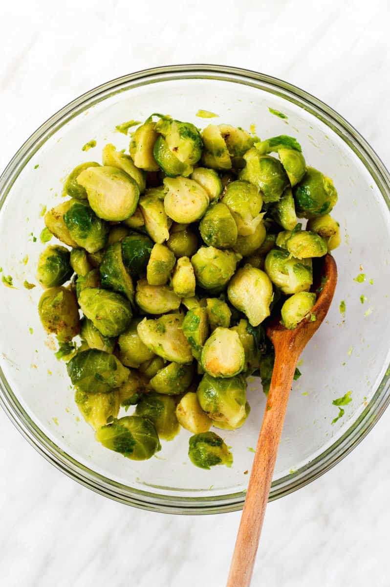 Brussels sprouts in a mixing bowl, tossed with spices and olive oil.