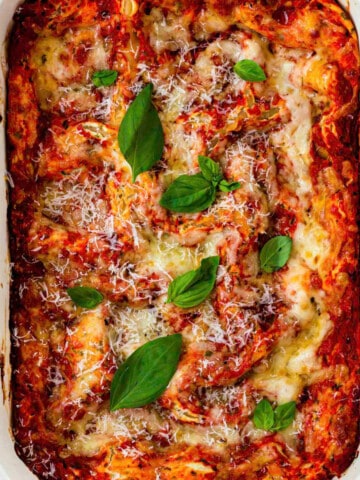 Three cheese lasagna in a ceramic baking dish topped with grated parmesan cheese and basil leaves.