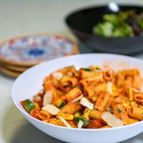 paccheri pasta and veggies in a white bowl with a fork in it.