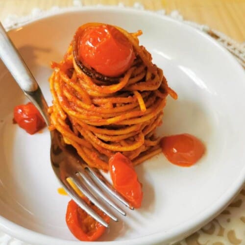 assasin's spaghetti on a white plate with a fork and topped with cherry tomatoes.