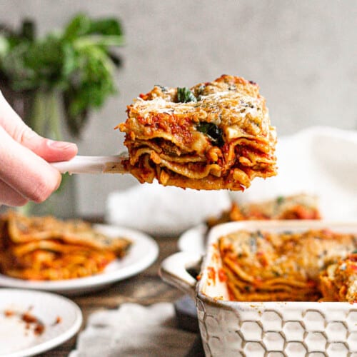 holding a piece of lasagna up after taking from casserole dish.