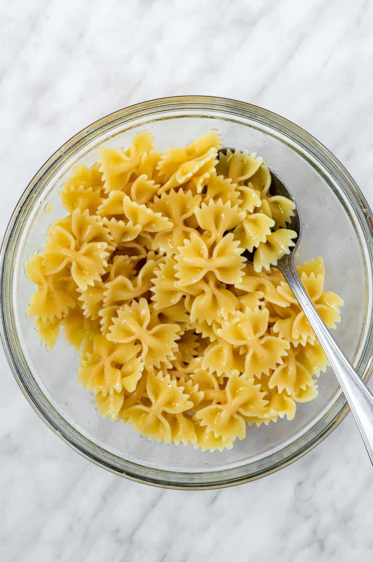 Cooked pasta tossed with olive oil in a mixing bowl.