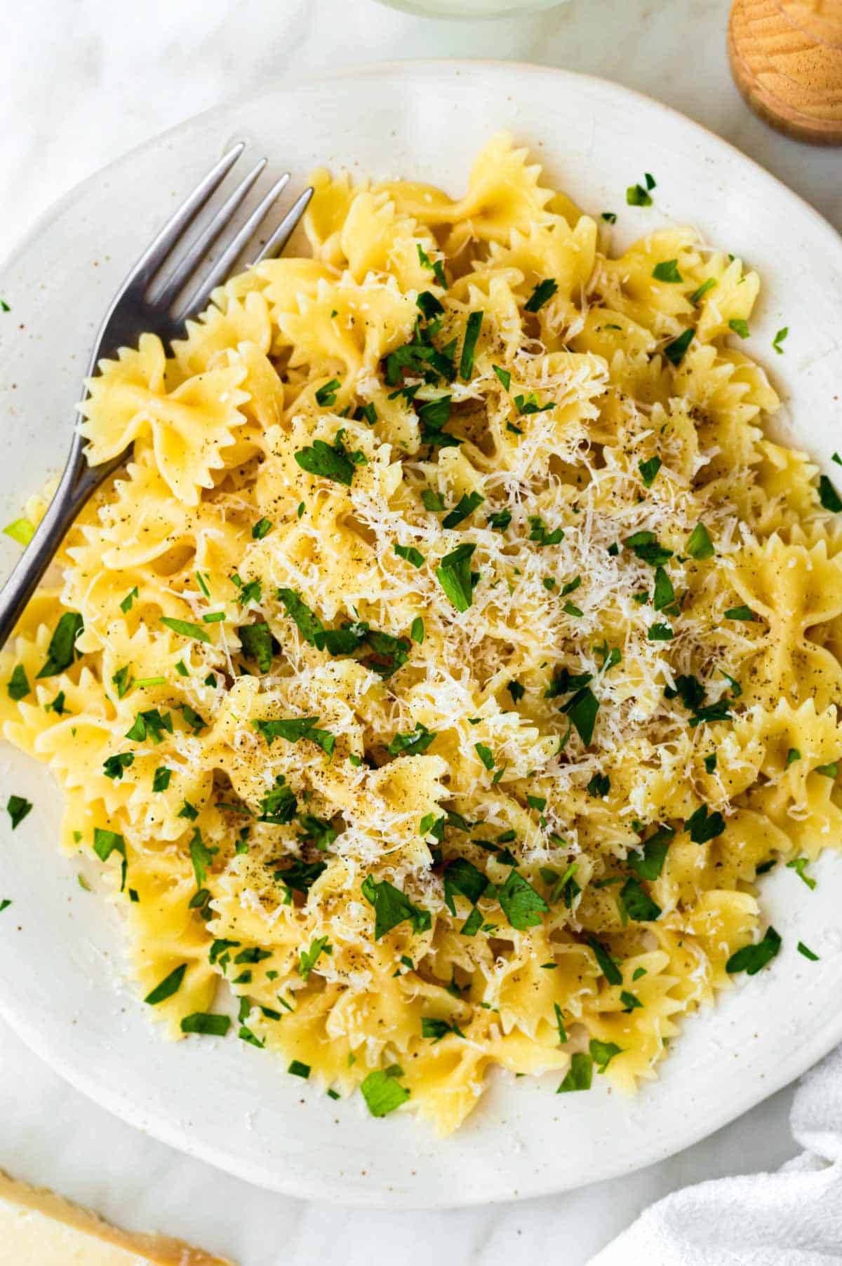 A close-up photo of cooked farfalle pasta served in a white plate and topped with parmesan cheese and parsley.