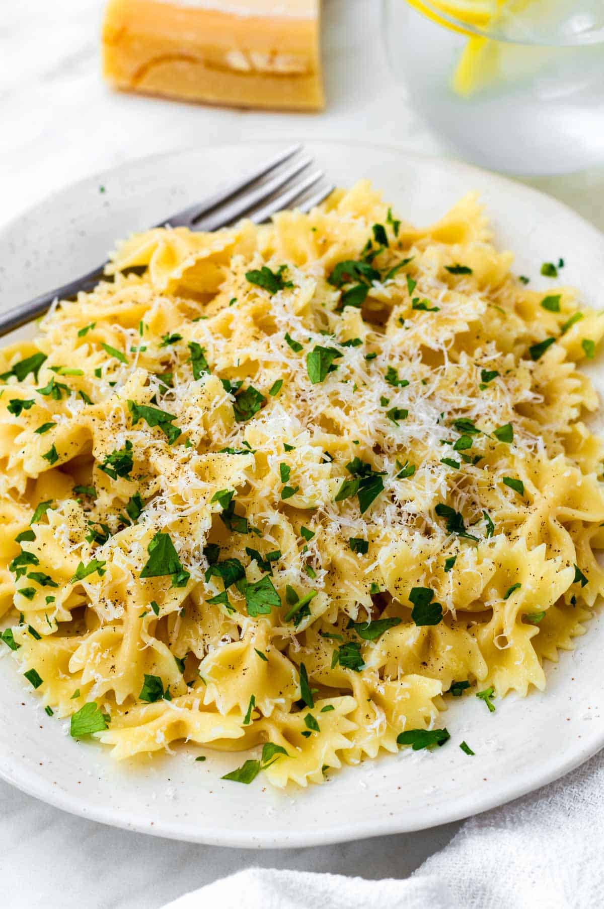 A white plate filled with pasta topped with parmesan cheese and fresh chopped parsley.