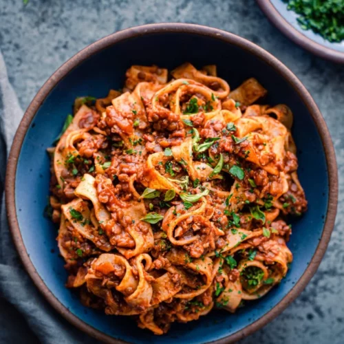 overhead of flat pasta with vegan bolognese sauce in a dark bowl.