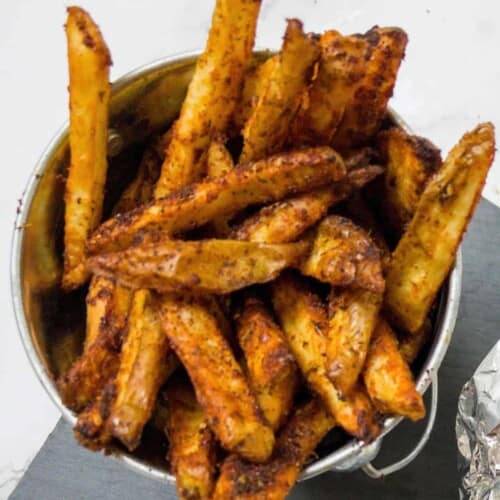 Close up of cajun fries in a small metal bucket.