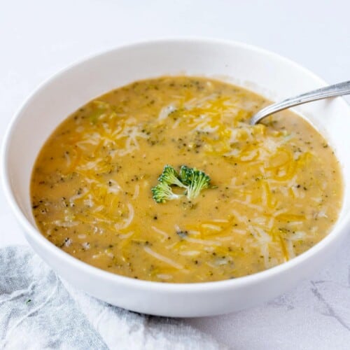 A silver spoon scoops a spoonful of instant pot broccoli cheddar soup out of a white ceramic bowl.