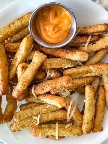 Air Fryer Frozen Zucchini Fries feature image 1200x1200. Fries set on a white plate served with chipotle sauce and garnished with parmesan cheese