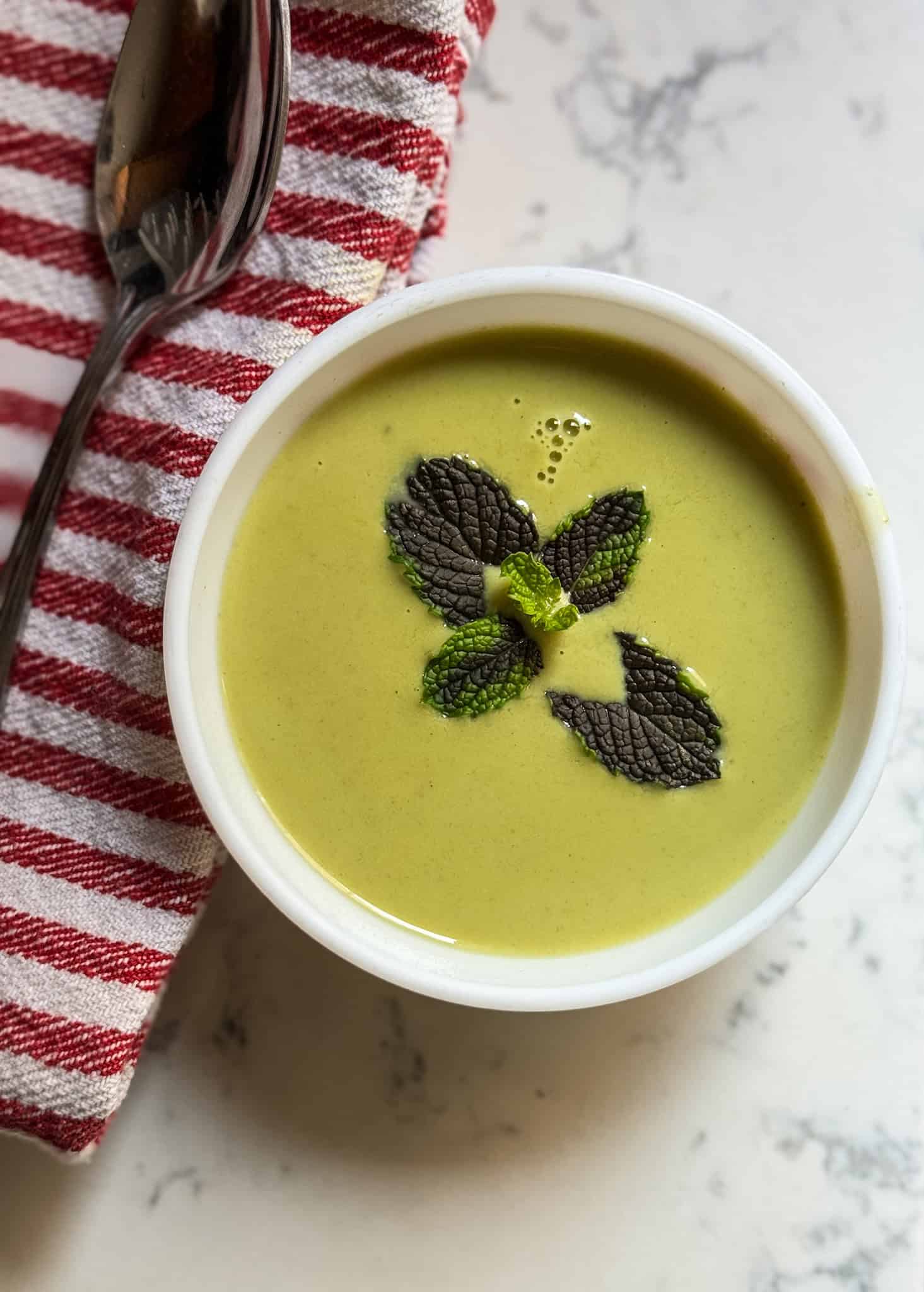 cucumber mint soup served in a bowl with mint garnish and spoon on the side 