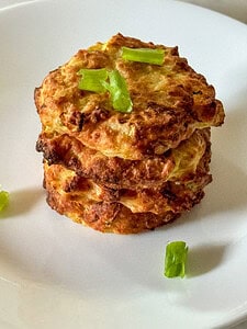 stack of four zucchini squash air fryer fritters garnished with green onions on a white plate